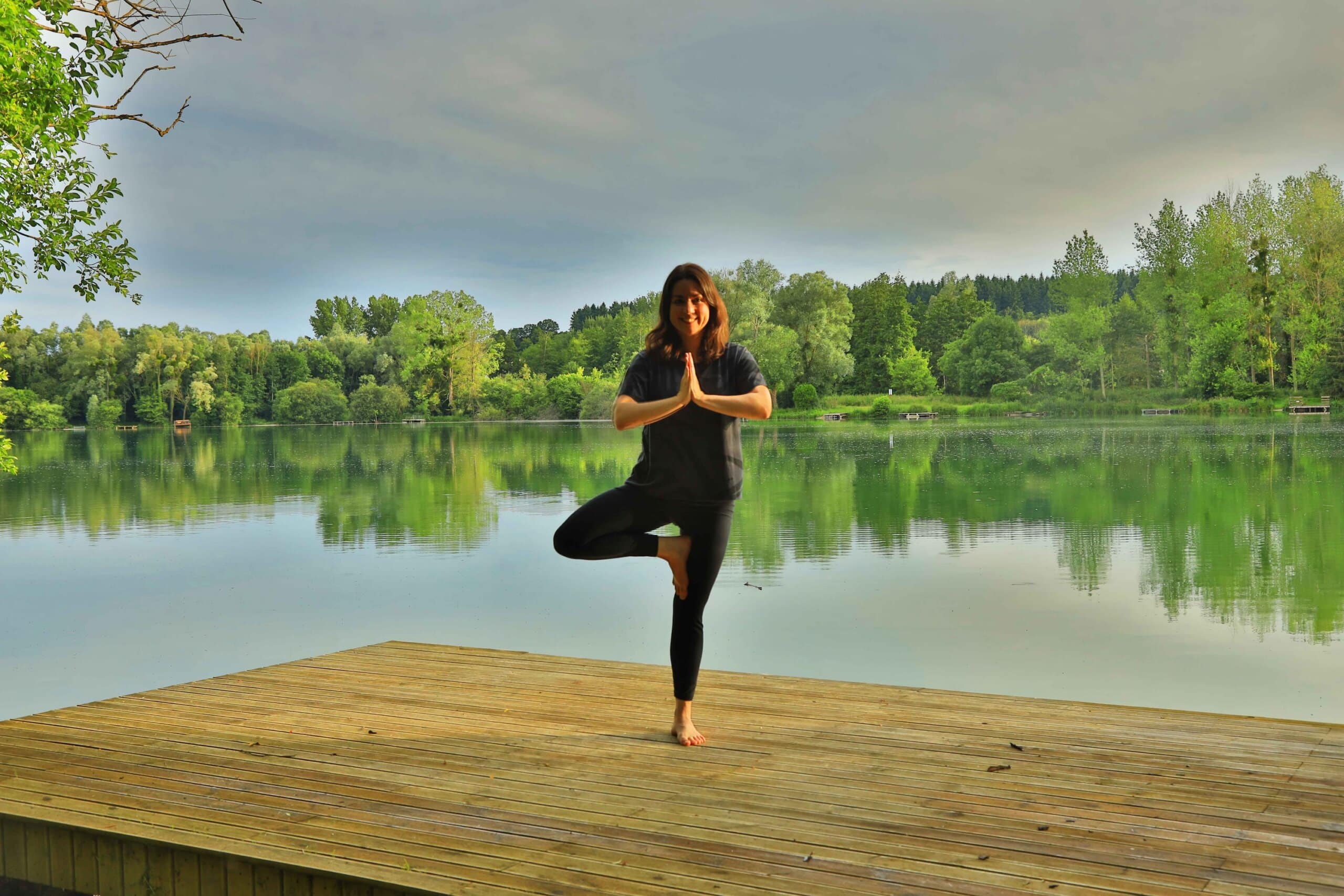 Dorinda Gilbert en posture de l’arbre au bord d’un étang, entourée d’arbres.